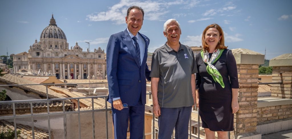 Three people stand and smile in front of an ancient building.