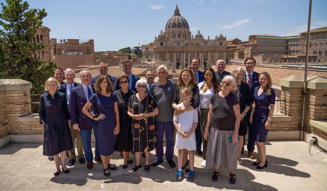 A large group of people smiles in front of an ancient building.