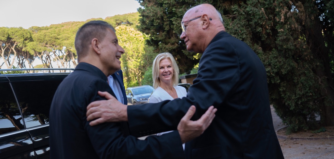 Two men wearing black coats embrace each other, while a woman framed in between them smiles.