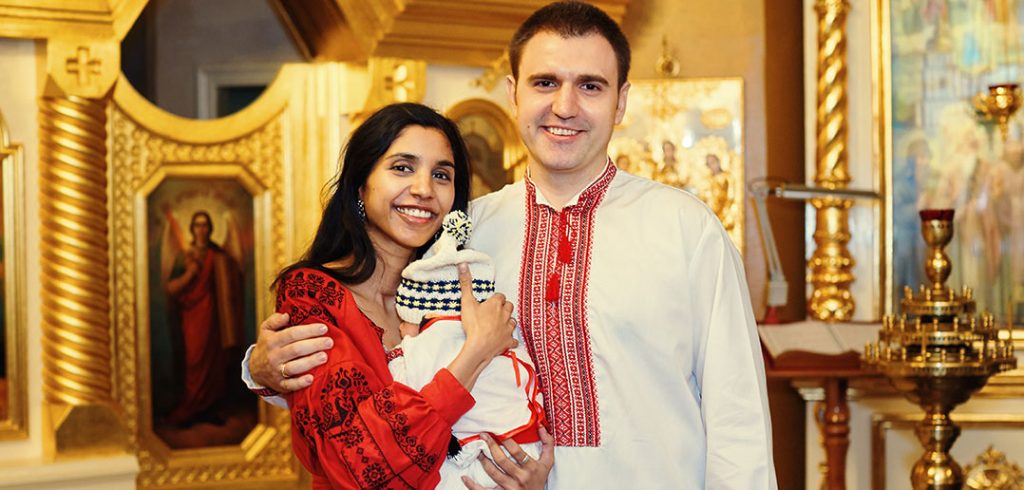 Fordham graduates Priya and Alex hold their infant son, Neil, in 2019 following Neil's baptism in St. Michael's Golden-Domed Cathedral in Kyiv.