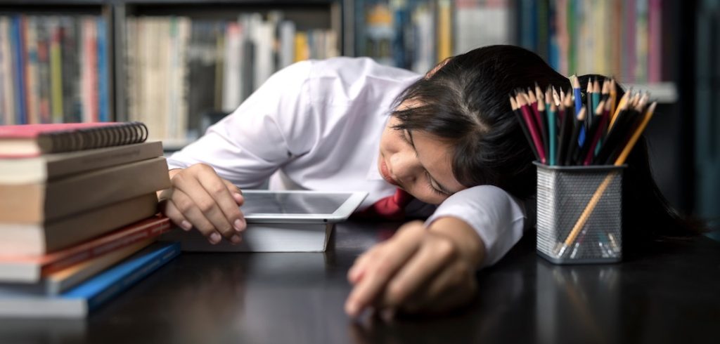 Student teen sleeping sit at table at library study online on laptop with textbook