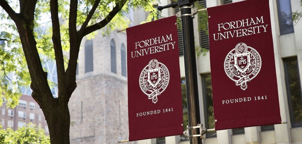 Two maroon flags saying "Fordham" hang in front of trees.