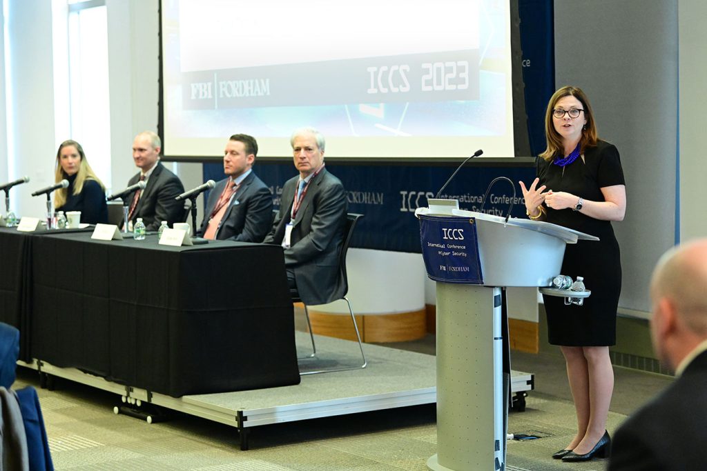 Fordham President Tanya Tetlow speaking from a podium while panelists at a table sit off to her right. 