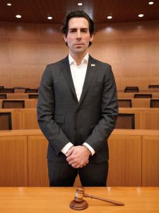 A man stands while holding his hands in front of him in a courtroom.