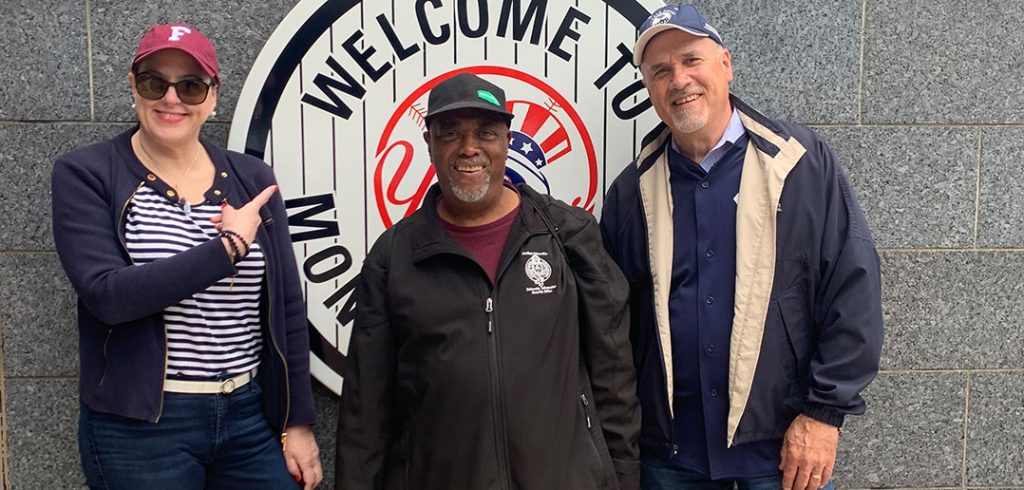 Calvin Graham standing between a man and a woman, in front of a Yankees logo