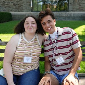 Two students sitting on an outdoor bench smile.