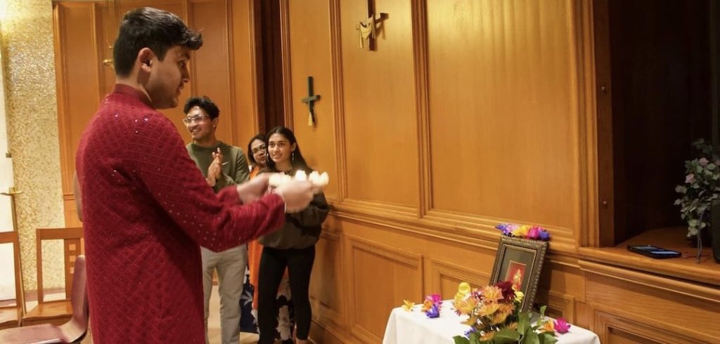 A man wearing South Asian garb offers a tribute to a table filled with flowers and gifts.