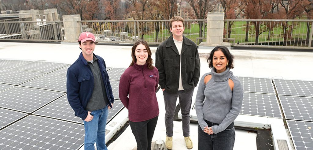 four students standing together, surrounded by solar panels