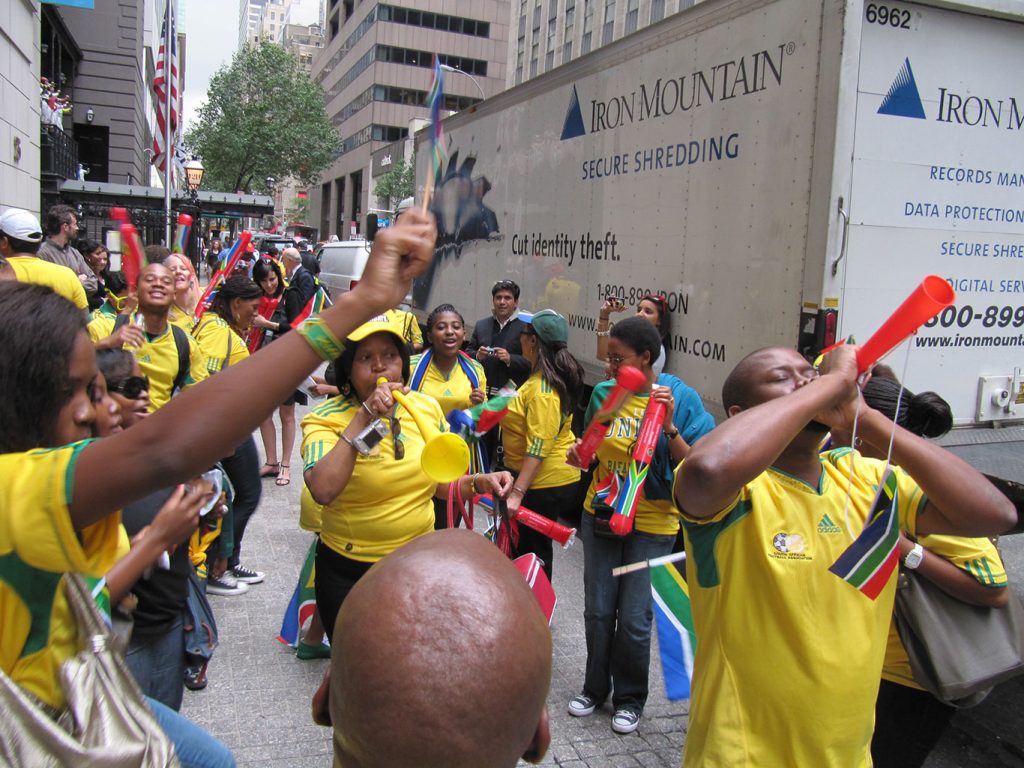 students celebrate on a sidewalk with horns and noisemakers