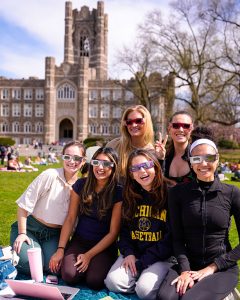 studnets posing for a picture in front of Keating Hall with eclipse glasses