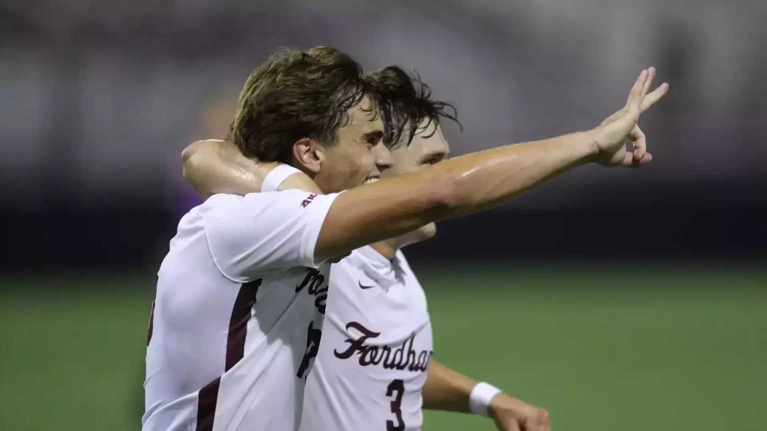 Two Fordham Men's soccer players smiling. One holding hand in air.