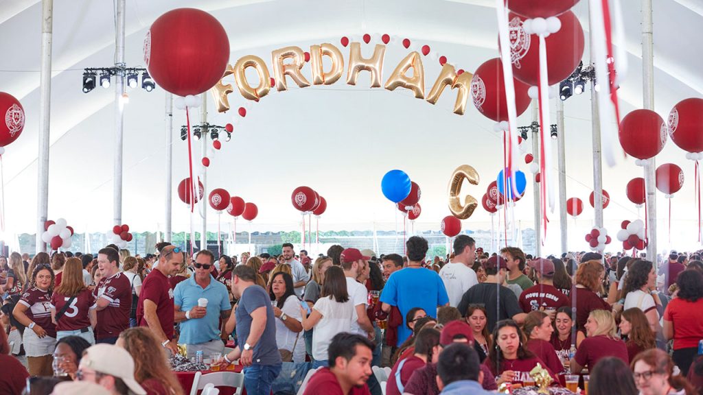 Alumni and families gather under the Homecoming tent with Fordham balloons. 