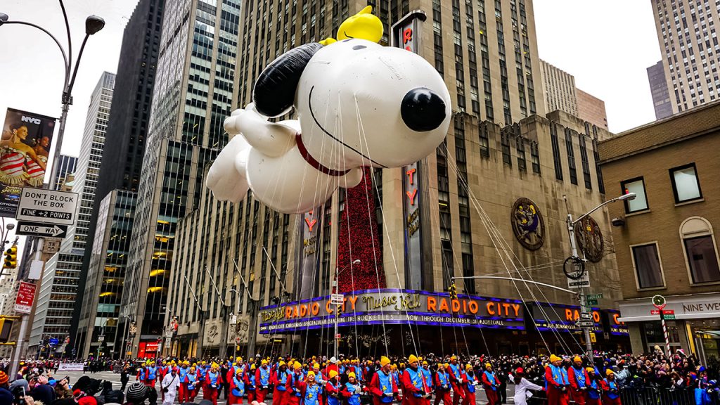 Snoopy balloon floats in the air during the annual Macy's Thanksgiving Day parade along Avenue of Americas with the Radio Music Hall in the background.