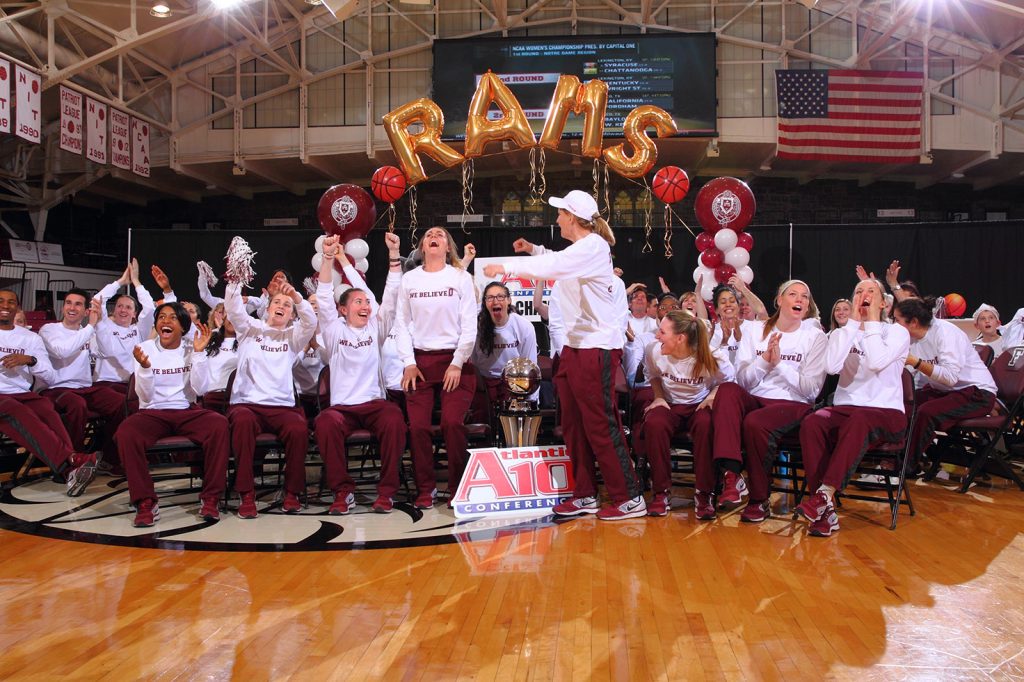 The 2014 Fordham women's basketball team sits on the Rose Hill Gym floor and cheers as they find out their opponent in the NCAA Tournament