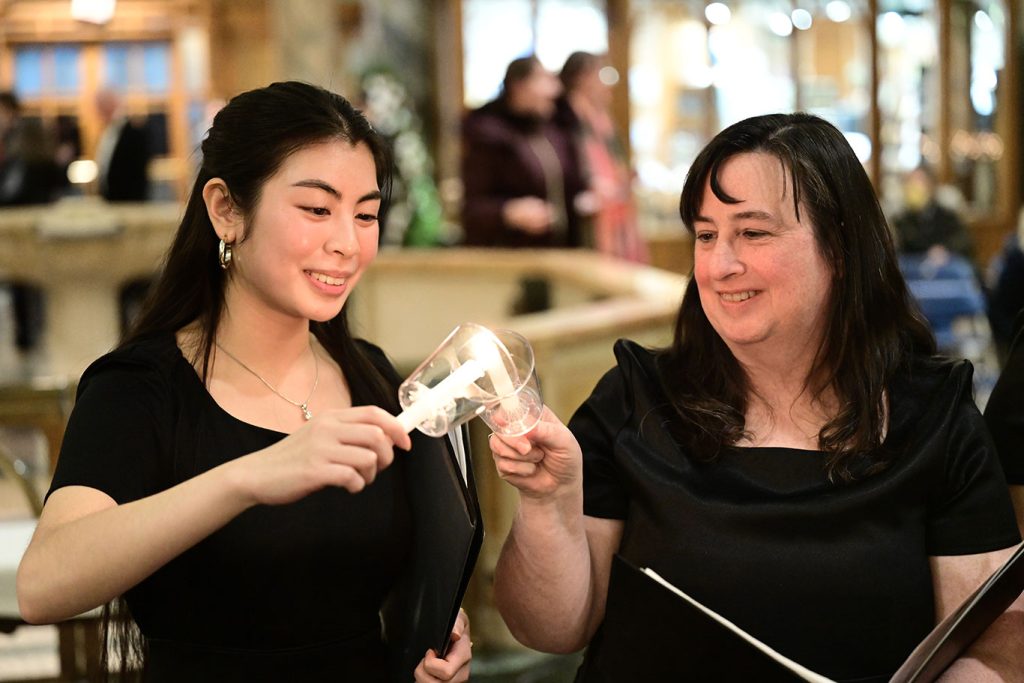 A woman holds out a candle for another woman to light hers.