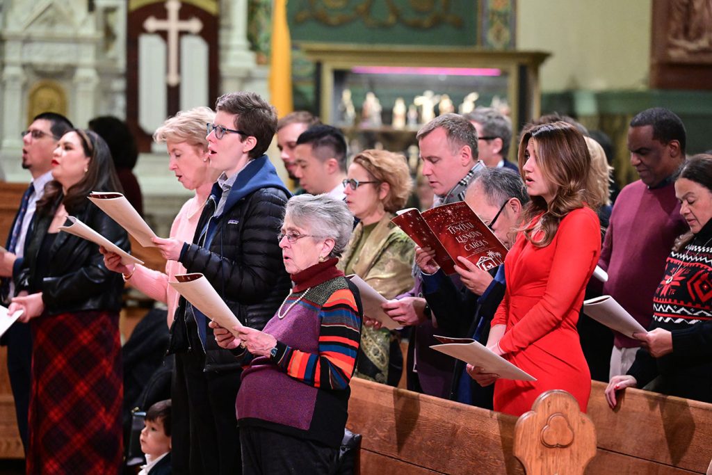 People standing together in pews, looking at songbooks and singing.