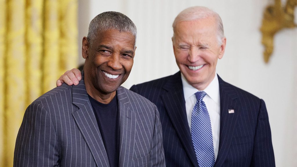 Denzel Washington smiles with U.S. President Joe Biden smiling behind him, a hand on Washington's shoulder.