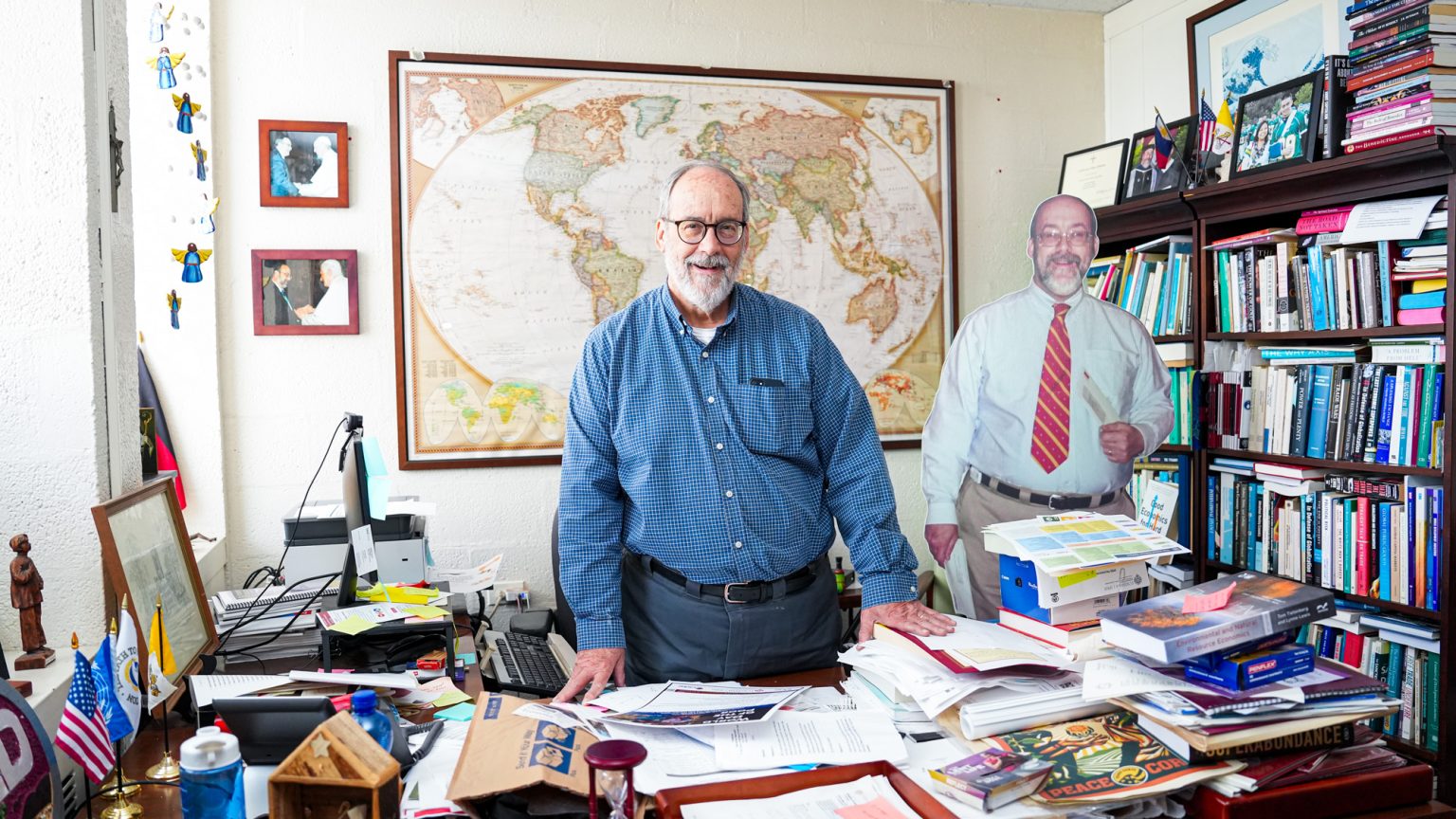 Henry Schwalbenberg stands and smiles in the center of his office.