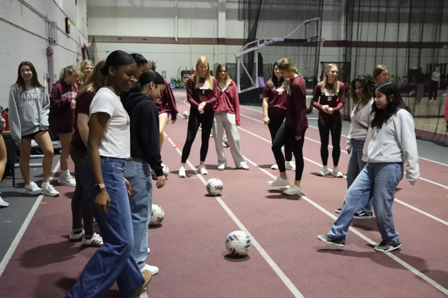 Young women standing in group, soccer balls on ground.