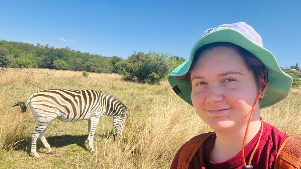 A person poses in front of a zebra, representing Fordham University as a top-producing institution for Fulbright students.