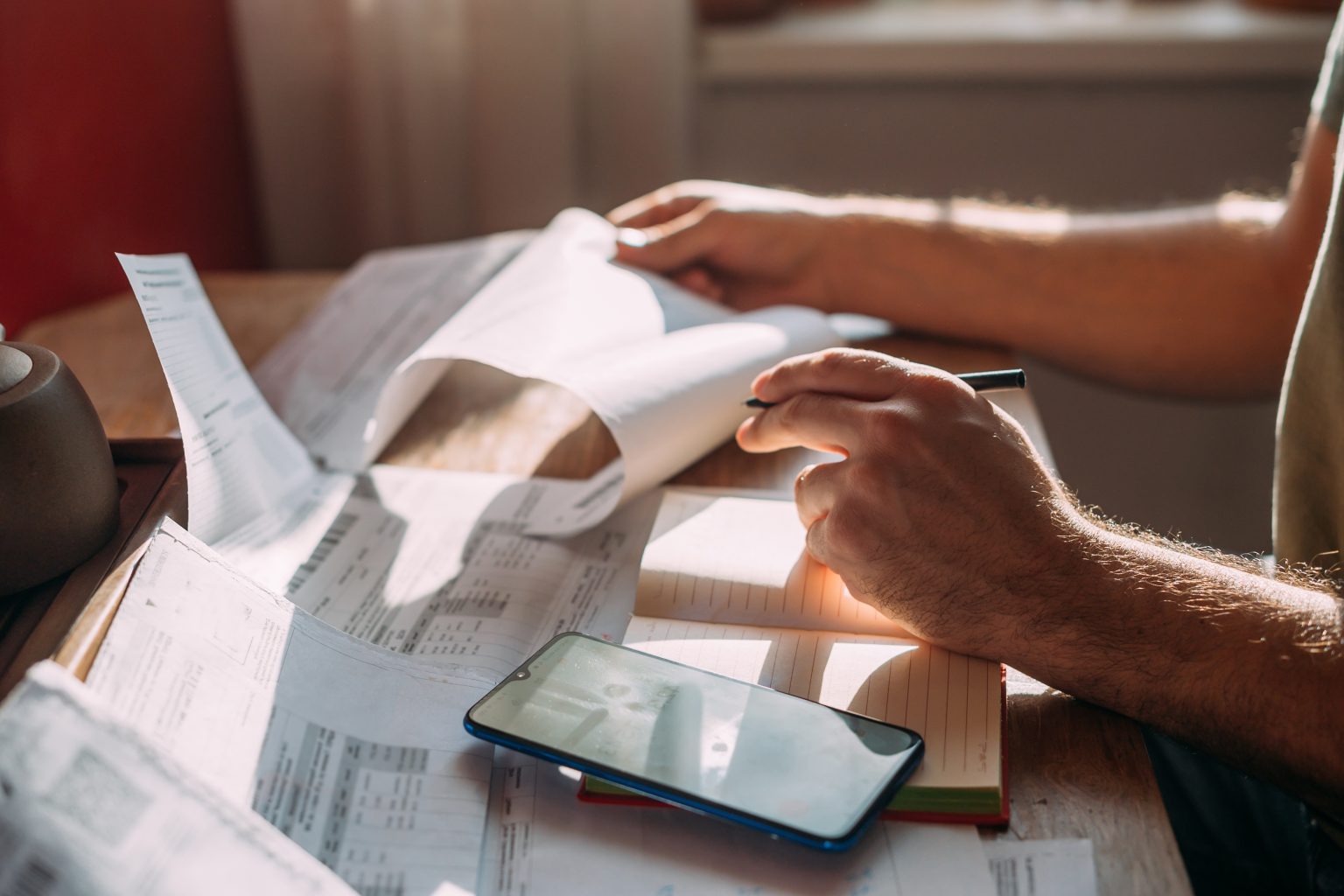 An image of a man's hands as he sorts through bills with a calculator, representing tariffs and their impact on inflation and consumer prices